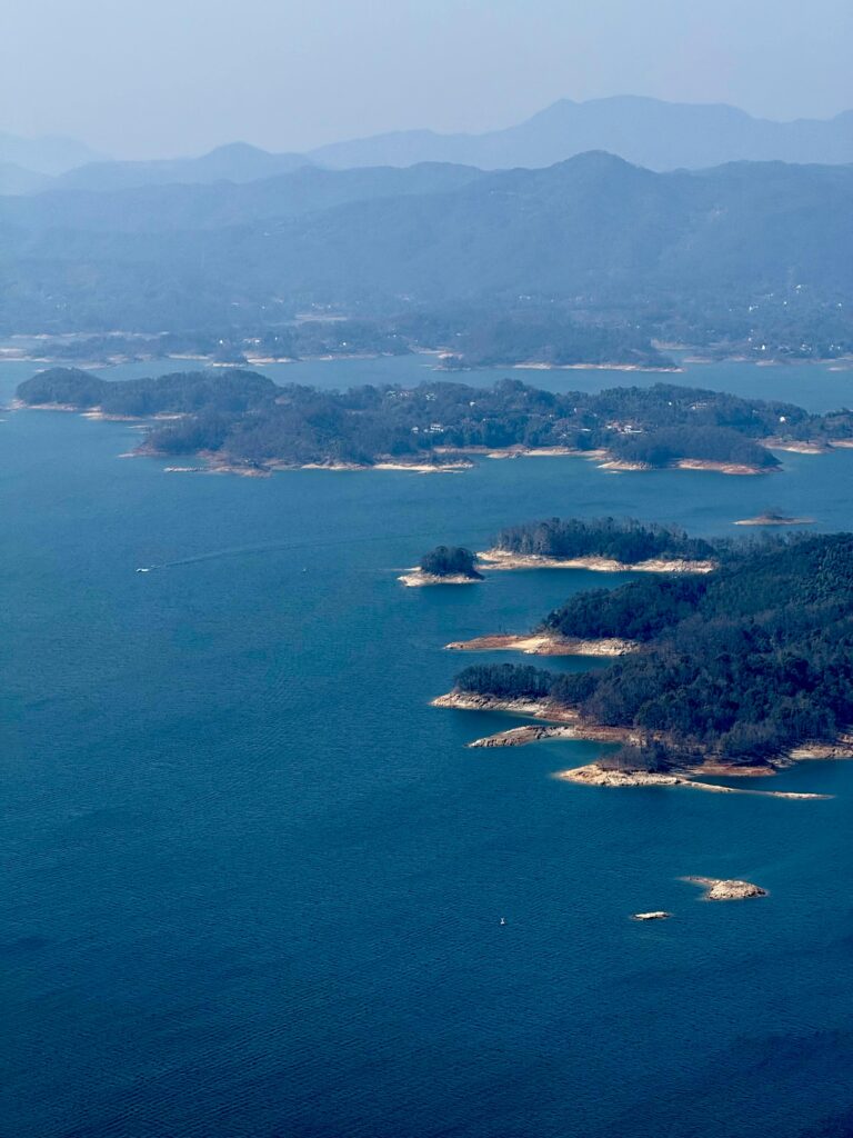 China Cultural Insights - Serene aerial view capturing lush green islands amidst expansive blue lakes surrounded by misty mountains.
